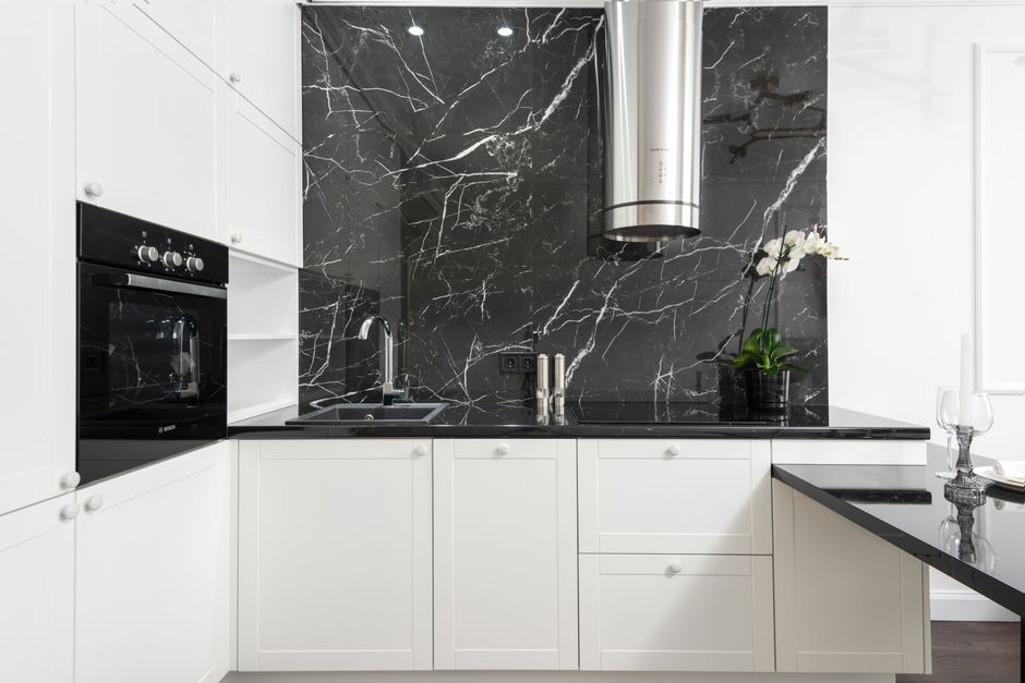 Sleek contemporary kitchen featuring white cabinets and black marble backsplash for a clean, minimalistic design.