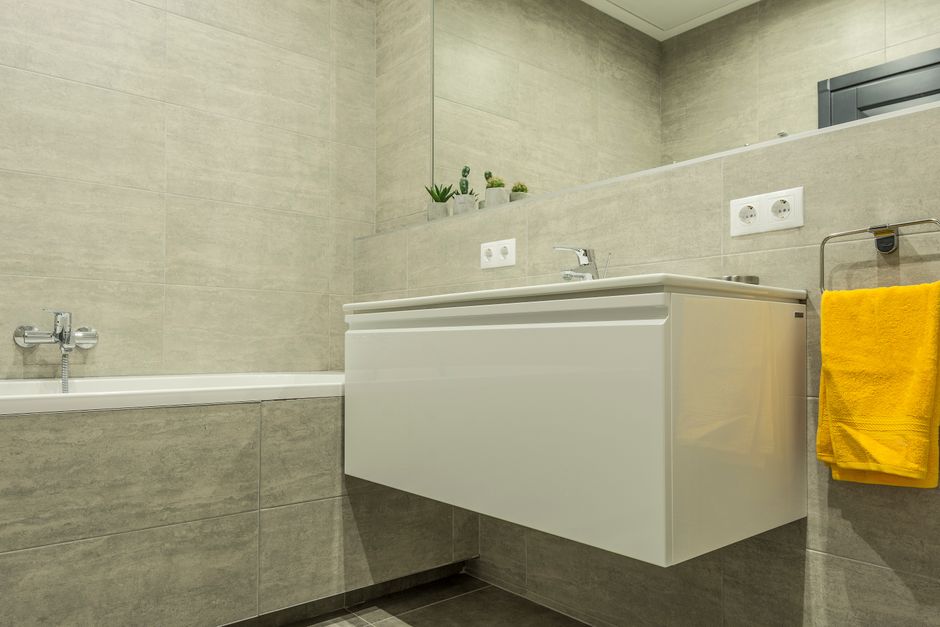Sleek modern bathroom with white sink, bathtub, and yellow towel accent.