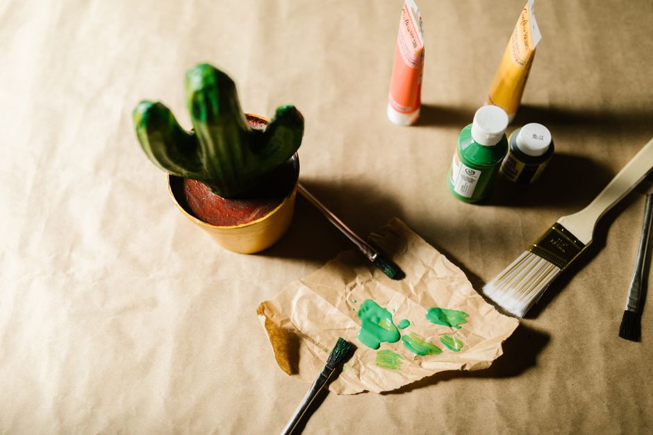 Colorful DIY painting project featuring a cactus pot, paint tubes, brushes, and vibrant creativity