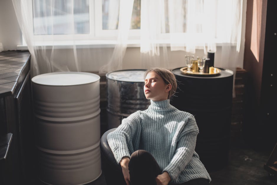 A young woman in a cozy sweater sits peacefully indoors, embracing natural light.