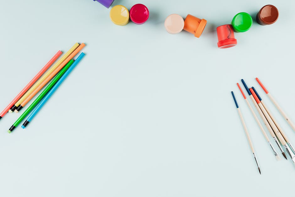 Flat lay of colorful art supplies, pencils, and brushes on a light background with copy space.