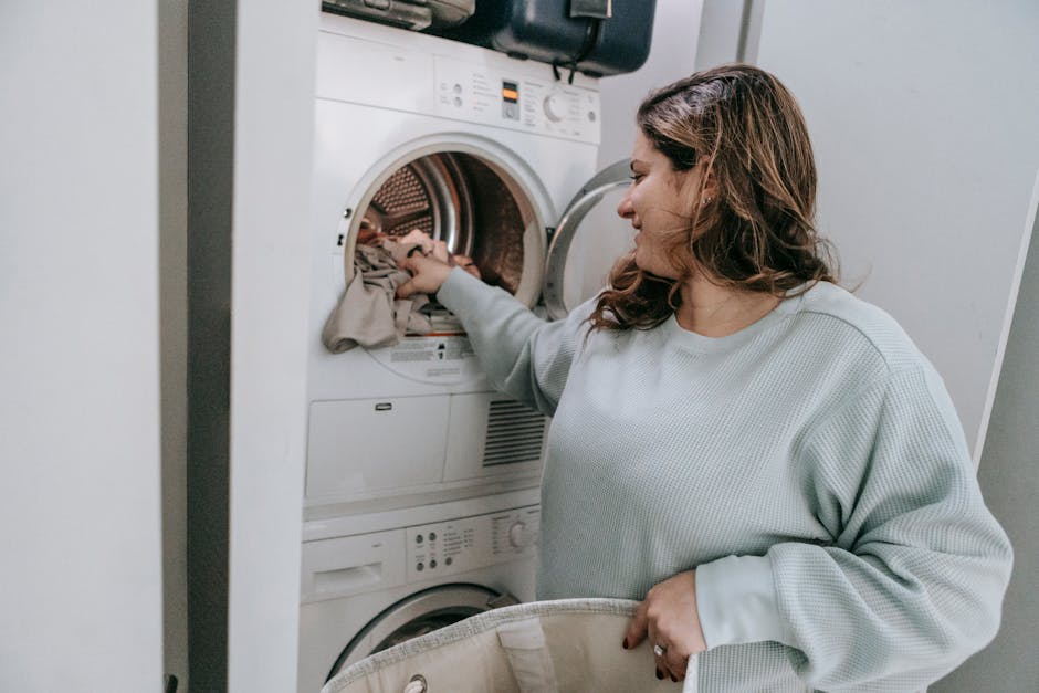 Glad female in casual wear loading dirt clothes in modern white washing machine while sitting in bathroom during household routine
