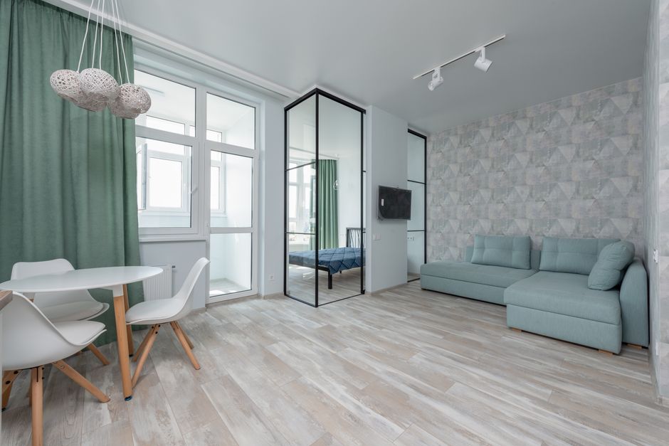 Interior of spacious flat with white table and chairs placed on parquet near wall against comfortable couch and bed at home