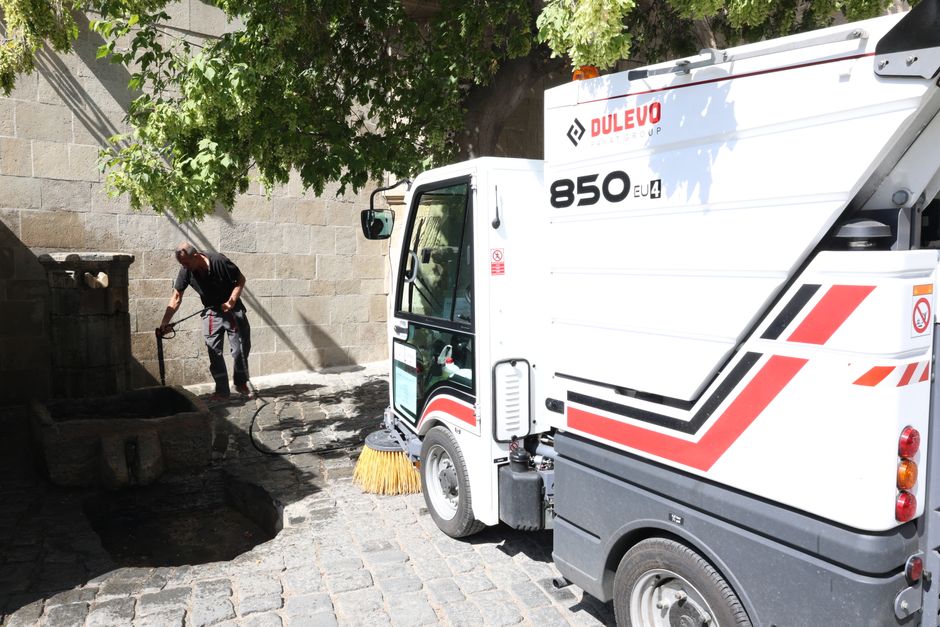 A worker cleaning a street with a mechanical sweeper on a sunny day.