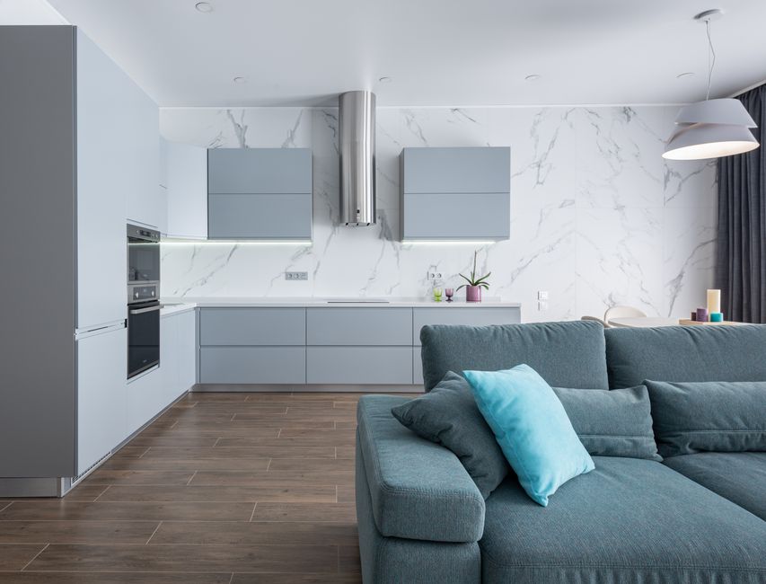 Interior of apartment with comfortable sofa and soft cushions in living room with open plan gray kitchen