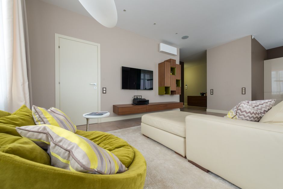 Comfortable white sofa placed against wall with TV and wooden shelf in spacious living room with green settee and cushions