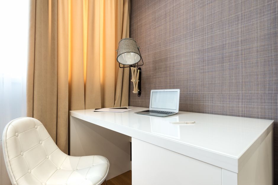 Laptop placed on white table near chair and wall with lamp in modern light workspace