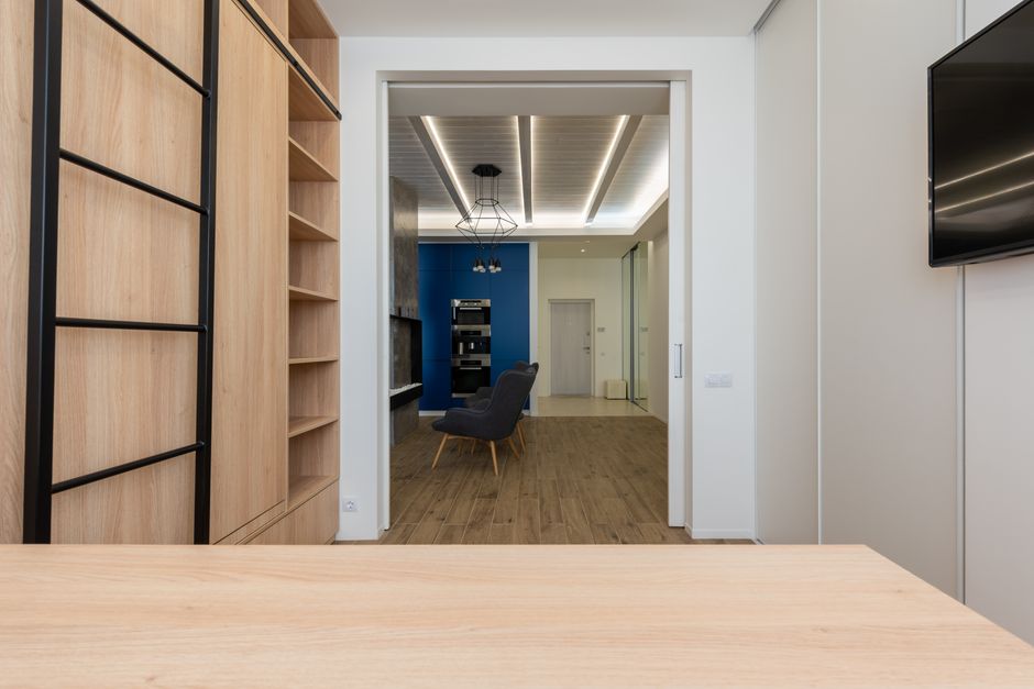 Interior of home office with wooden table and closet equipped with TV set and stylish kitchen