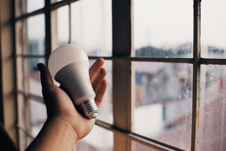 Anonymous person holding energy efficient light bulb in hand on blurred background of big dusty window in light room