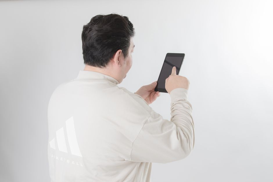 Man with black hair using a tablet on a white background, focusing on the screen.