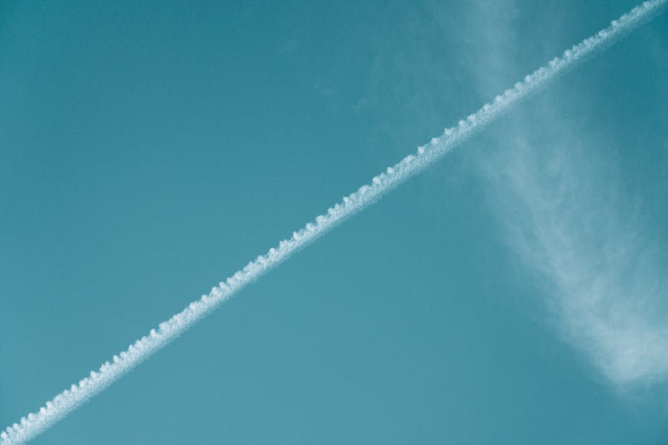 Airplane contrail streaking across a vibrant blue sky with wispy clouds.