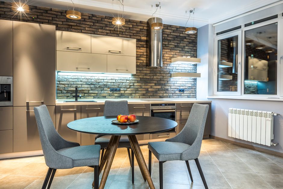 Contemporary kitchen interior with round table and chairs, featuring brick wall accents and sleek cabinetry.