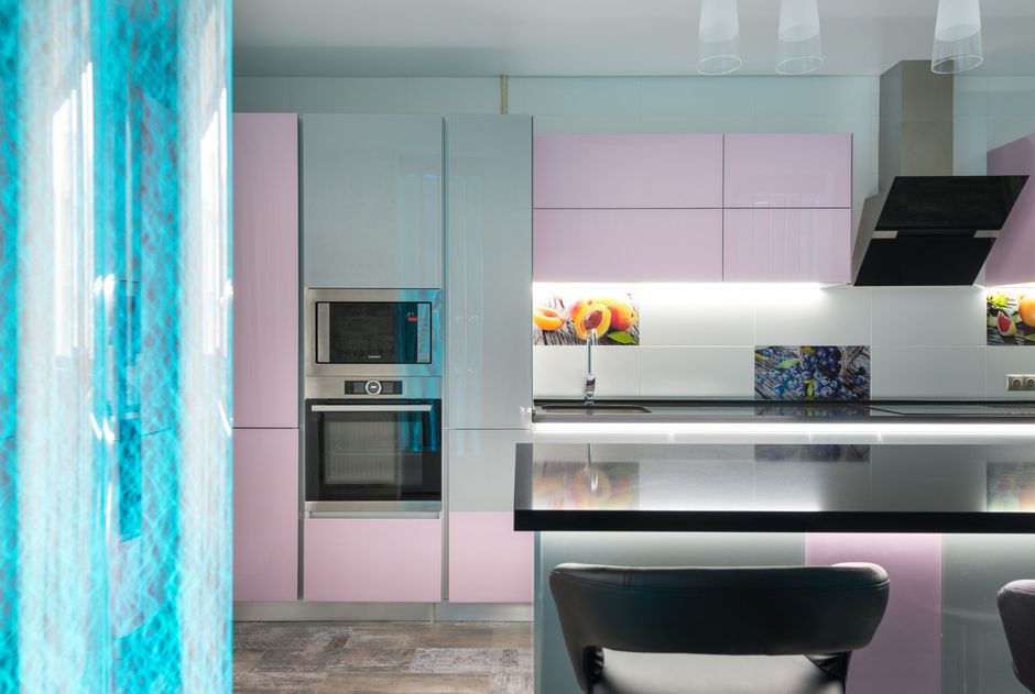 Black kitchen counter with chairs placed near colorful cupboards and contemporary appliances in stylish apartment with decorative blue bubble wall