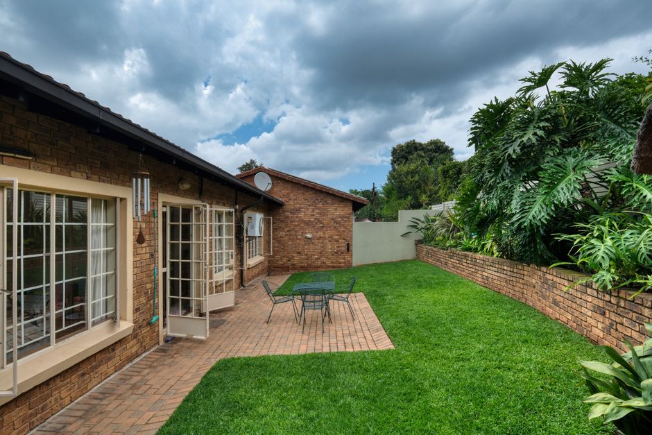 Cozy backyard with patio seating, lush grass, and beautiful foliage under a cloudy sky.