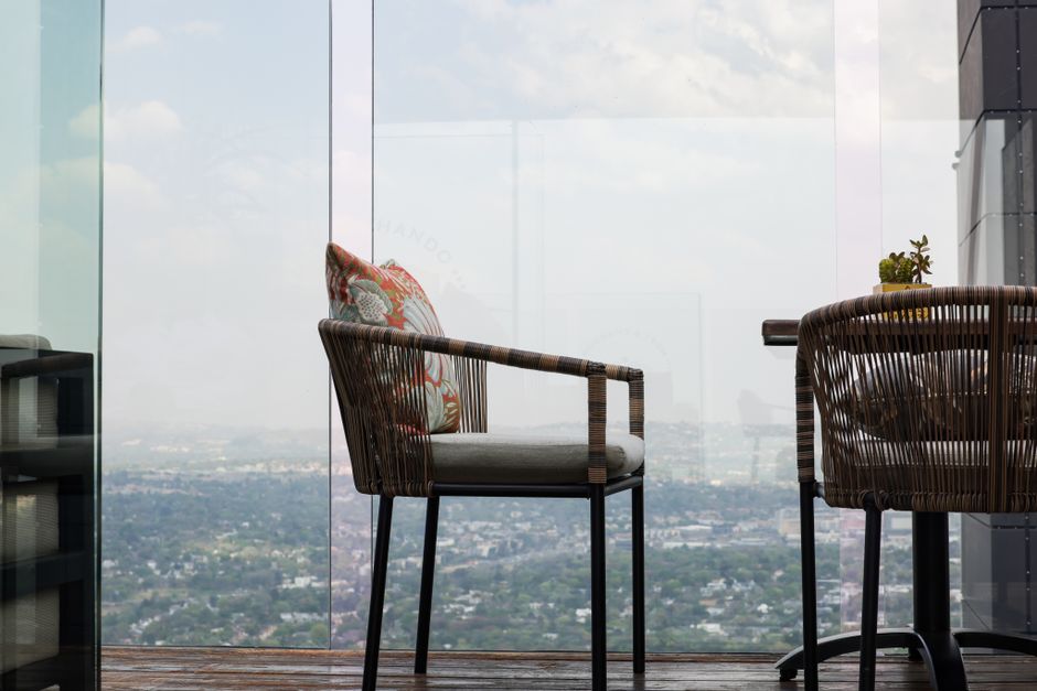 Elegant wicker chairs on a glass skydeck overlooking a sprawling cityscape.