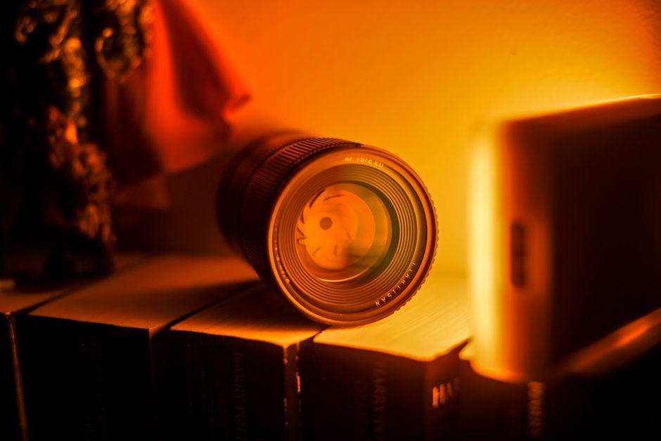 A photography lens resting atop books, illuminated by warm orange lighting, creating a cozy ambiance.