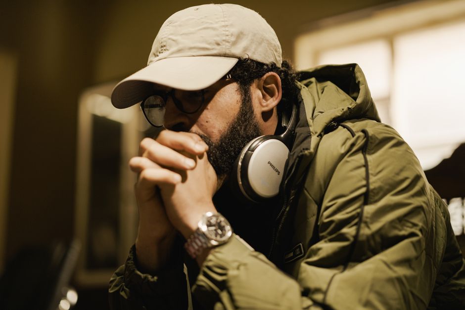 A man wearing headphones and a green jacket, deep in thought indoors. Captures introspective mood.