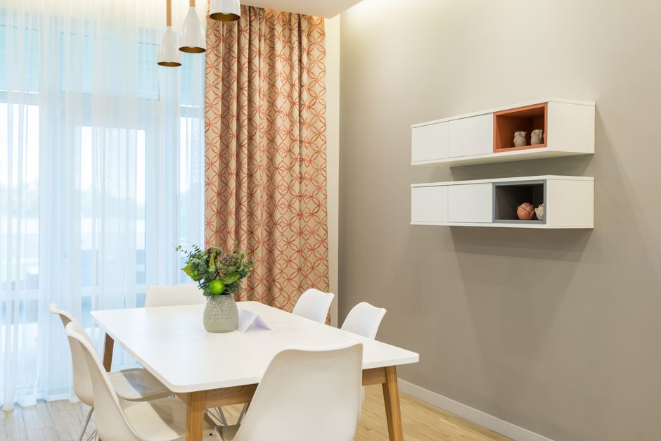 Green flowers in vase placed on white table with chairs near window and wall decorations on shelves in light room