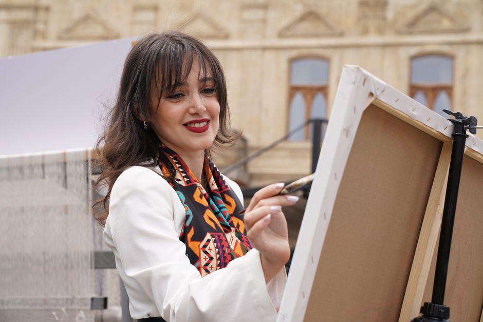 A female artist painting outdoors in Baku, showcasing creativity and art in a cultural setting.