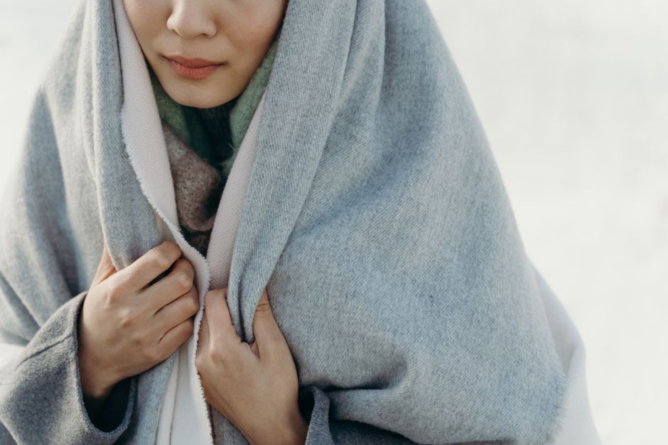 Close-up of woman wrapped in a gray shawl, highlighting comfort and warmth in a soft, minimalist setting.