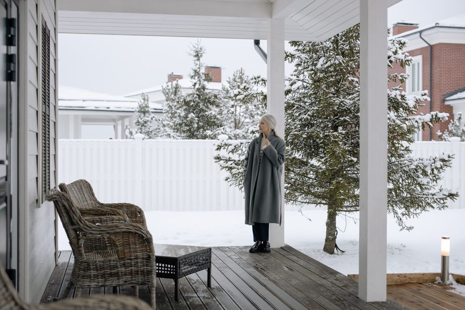 Elegant senior woman standing on a snowy porch, gazing afar in winter.