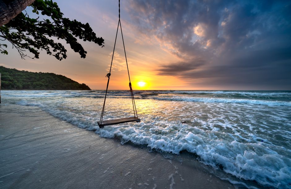 A tranquil beach scene with a swing overlooking the ocean during a vibrant sunset.