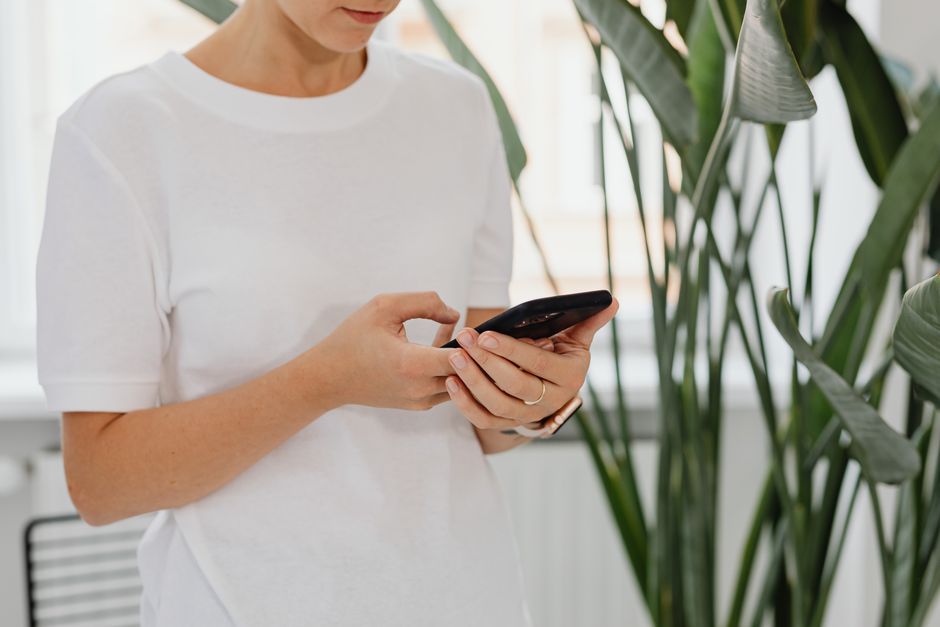 A woman uses a smartphone indoors surrounded by lush green plants.