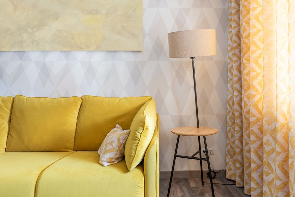 Contemporary room interior with cushions on sofa against lamp and curtain with ornament at home